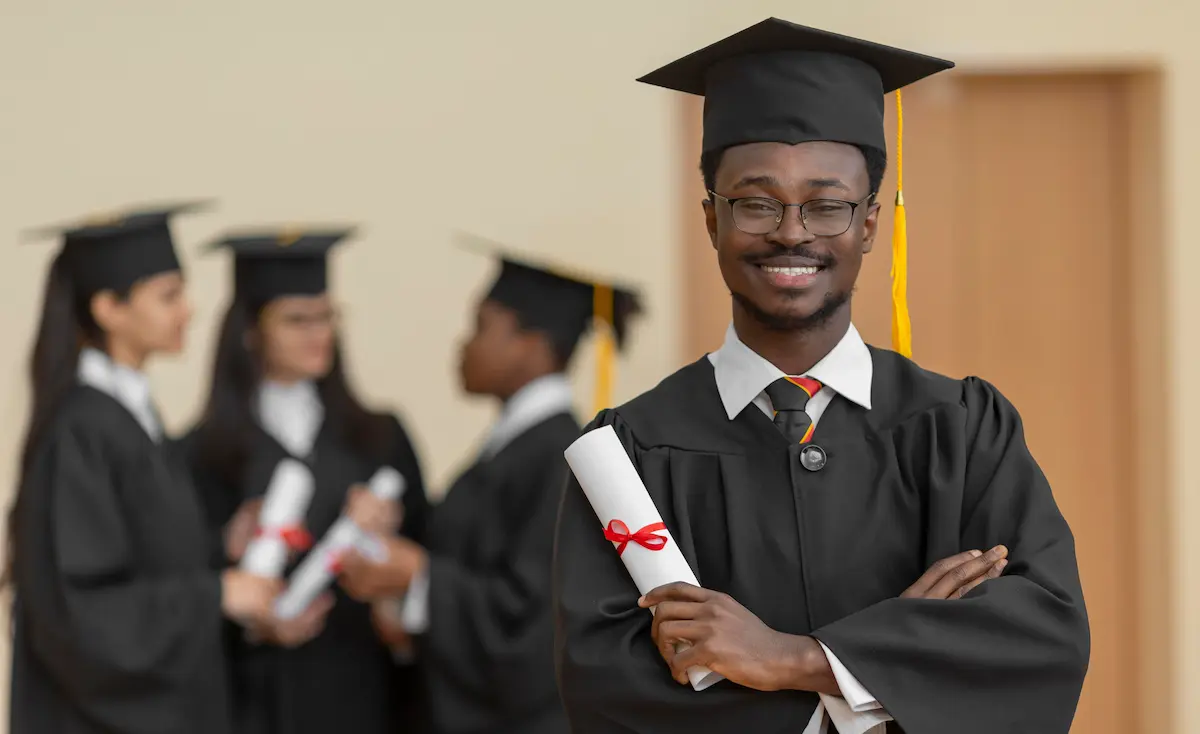 A smiling graduate in full cap and gown holding a diploma, celebrating completion of an online master’s degree